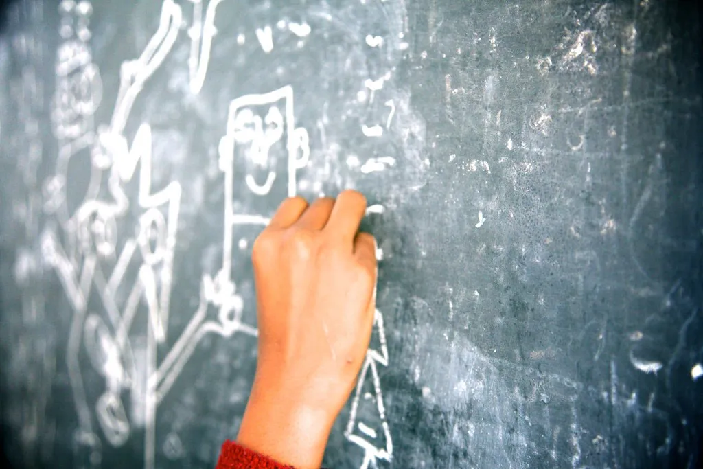 A hand adding a chalk line to a drawing on a blackboard.
