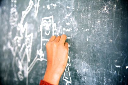 A hand adding a chalk line to a drawing on a blackboard.