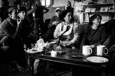 A black and white photograph of adults around a table with mugs.