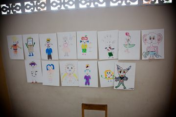 Fourteen drawings of characters taped to a wall in two rows.