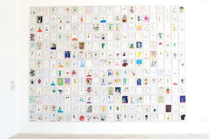 A white gallery wall hung with hundreds of alien drawings in a tight grid.