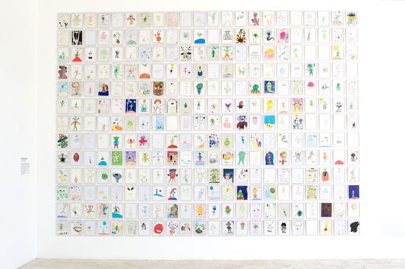 A white gallery wall hung with hundreds of alien drawings in a tight grid.