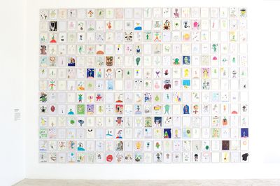 A white gallery wall hung with hundreds of alien drawings in a tight grid.