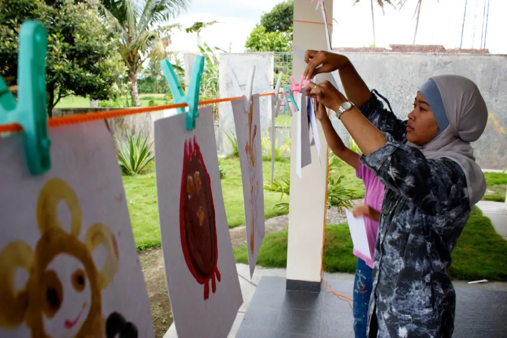 Alien drawings pegged to a line outdoors while a child hangs another.