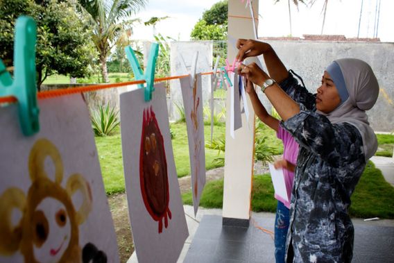 Alien drawings pegged to a line outdoors while a child hangs another.