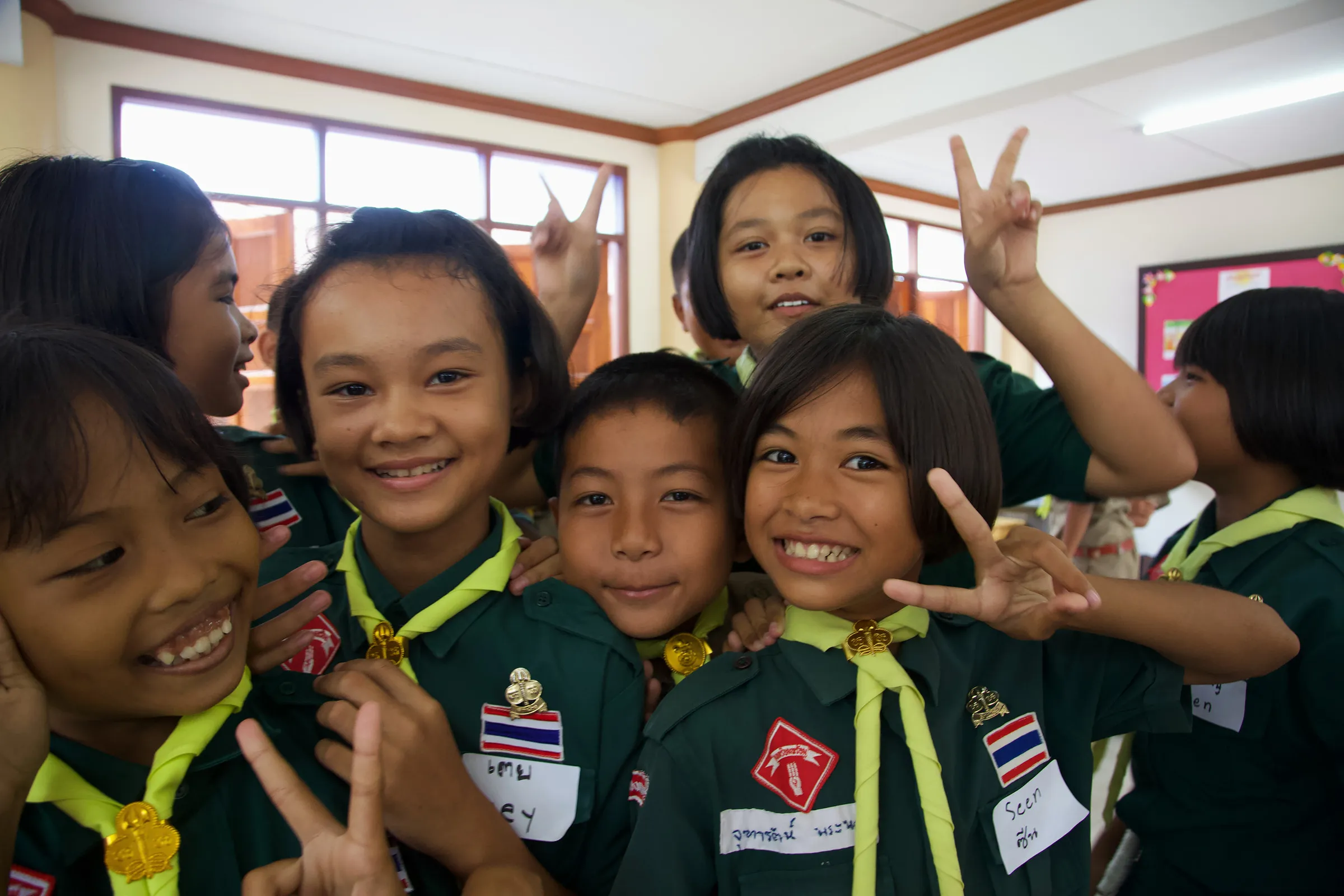 Children in green school uniforms crowding together and making hand signs at the camera.