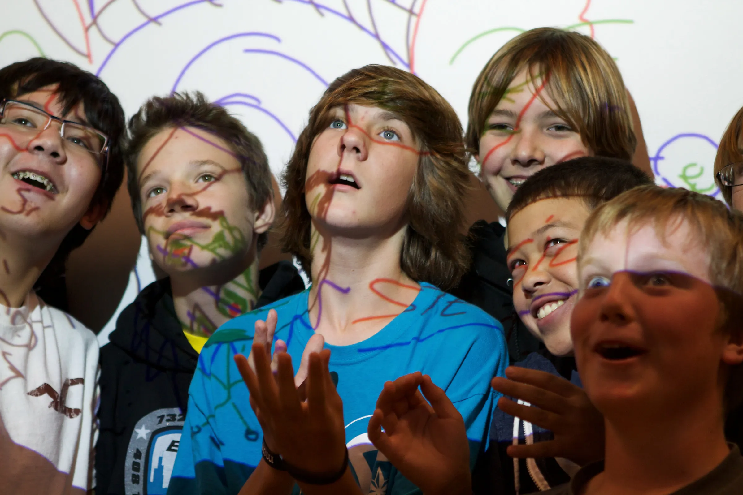 Children's faces with coloured drawn lines projected across them.