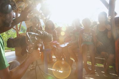 Sound recording equipment and children seated in a sunlit shelter.