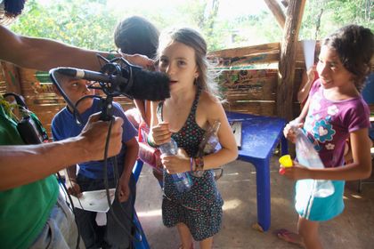 A child speaking into a boom microphone held by an adult.