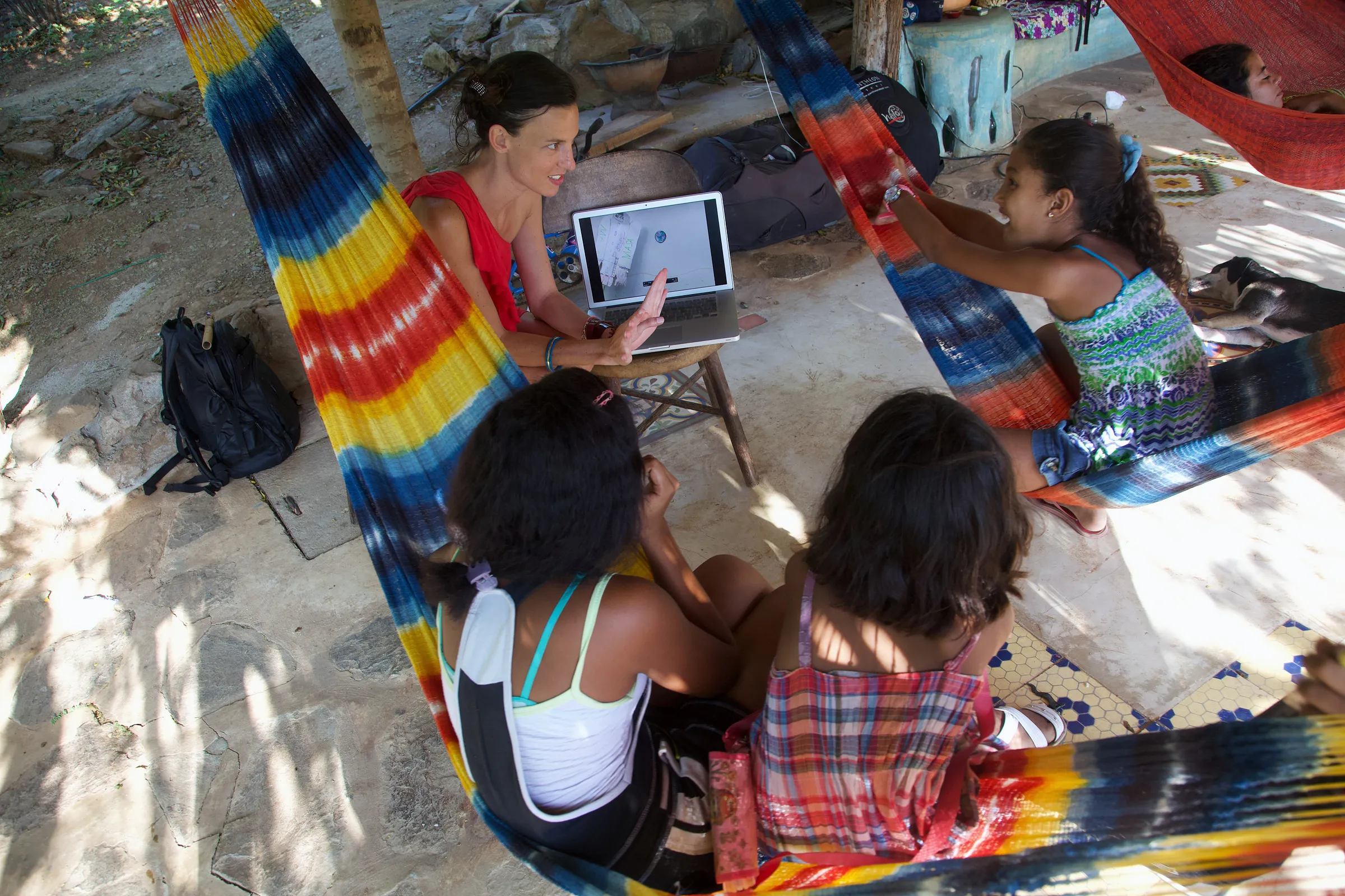 Children and adults with a laptop among colourful hammocks.