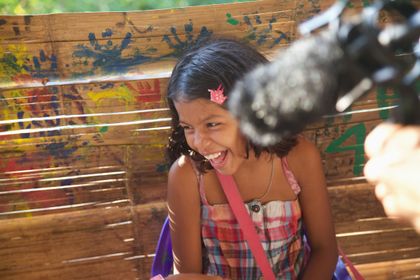 A child laughing beside a boom microphone, with painted handprints on the wall behind.