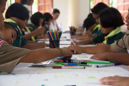 Children drawing with felt pens along a long table.
