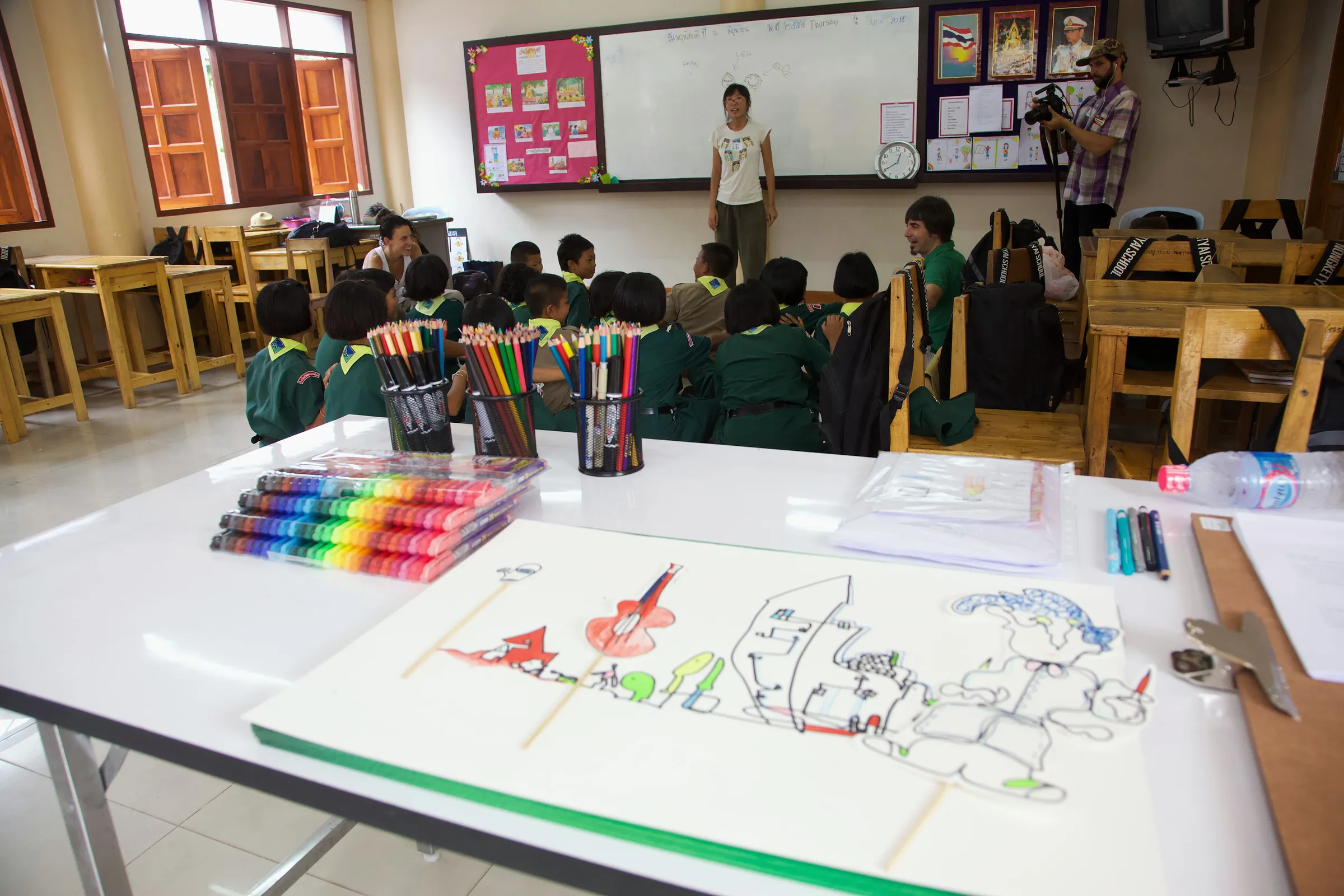 A classroom with a large drawing of figures and vehicles on a table in the foreground.