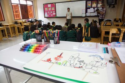 A classroom with a large drawing of figures and vehicles on a table in the foreground.