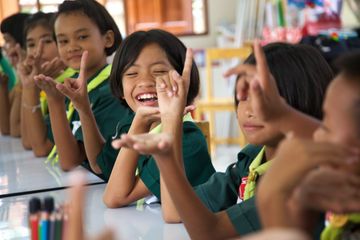 Children at a table laughing and making hand signs.