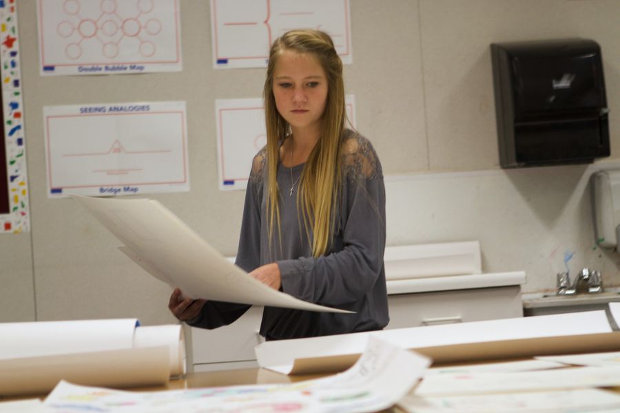 A teenager holding a large sheet of paper in a classroom.