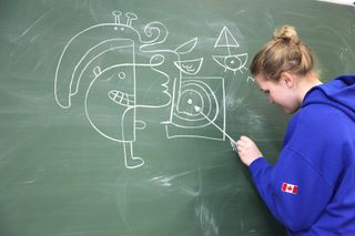 A girl in a blue hoodie adds to a large chalk drawing on a blackboard. Brandenburg, Germany, 2010.