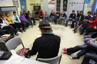 A man in a hat at a loop machine, students listening in a circle around him. Brandenburg, Germany, 2010.