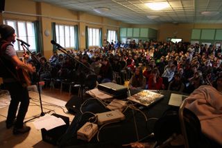 A musician with a guitar plays to a full hall of students. Brandenburg, Germany, 2010.