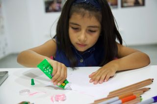 A girl squeezes green glue onto her paper, coloured pencils beside her. Barcelona, Spain, 2010.