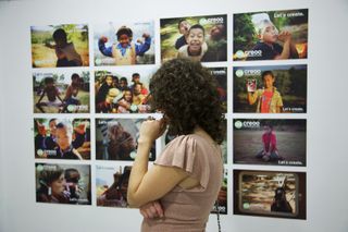 A woman looks at a wall of colour photographs of children. Barcelona, Spain, 2010.
