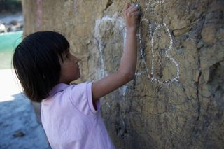 A girl draws with chalk on a big rock by a river. The Ideal Place, 2011.
