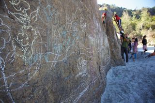 A rock face covered in white chalk drawings, children further along. The Ideal Place, 2011.