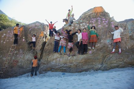 Children stand and climb across painted boulders on a sandy riverbank. The Ideal Place, 2011.