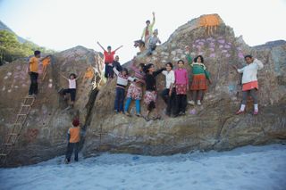 Children stand and climb across painted boulders on a sandy riverbank. The Ideal Place, 2011.