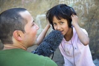 A man holds a furry microphone to a girl wearing headphones. The Ideal Place, 2011.