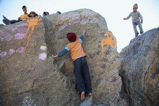 A boy climbs a painted boulder while another child stands on top. The Ideal Place, 2011.