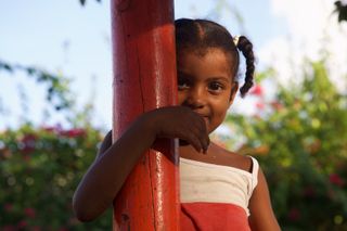 A girl looking out from behind a red wooden post. Barú, Colombia, 2011.