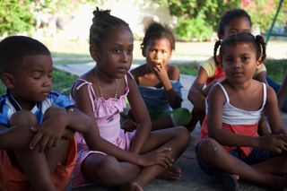 Children sitting on the ground in a circle, one girl in a pink dress. Barú, Colombia, 2011.