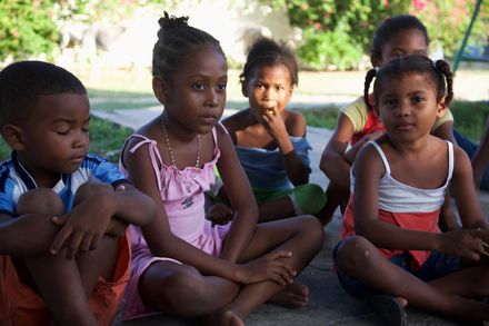 Children sitting on the ground in a circle, one girl in a pink dress. Barú, Colombia, 2011.