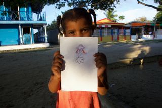 A girl on a sandy street holds up her drawing of an alien. Barú, Colombia, 2011.