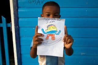 A boy holds up his striped alien drawing in front of a blue door. Barú, Colombia, 2011.