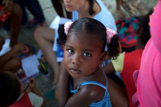 A small girl with pink hair ties looks up, other children drawing around her. Barú, Colombia, 2011.