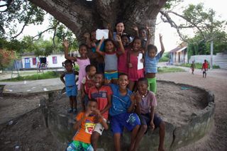 A crowd of children waves from the stone base of a huge tree. Barú, Colombia, 2011.