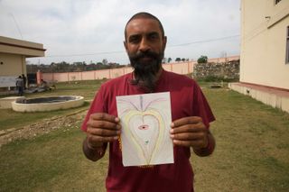 A bearded man holds up a drawing of a heart-shaped form with an eye. Rishikesh, India, 2012.