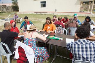Adults drawing together at tables set out on a lawn. Rishikesh, India, 2012.