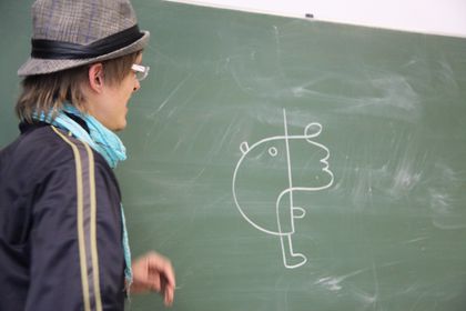 Ole Ukena in a hat and glasses, turning from a chalkboard with a line drawing of a figure.