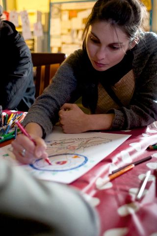 A woman draws a blue circle with a red pen at a table. Spain, 2012.