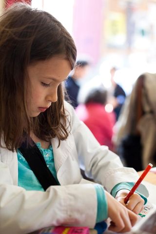 A girl draws with a red pen, looking down at her paper. Spain, 2012.