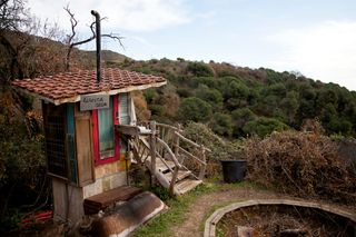 A small wooden hut with a tiled roof on a hillside covered in trees. Spain, 2012.