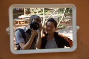 Two young people reflected in a mirror, one holding a camera.