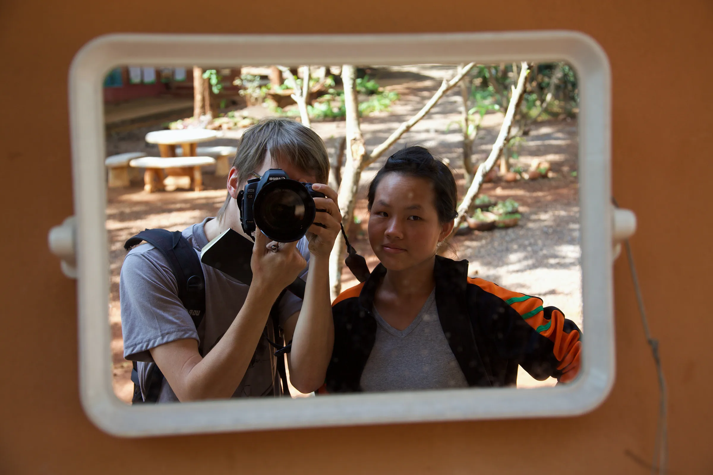 Two young people reflected in a mirror, one holding a camera.