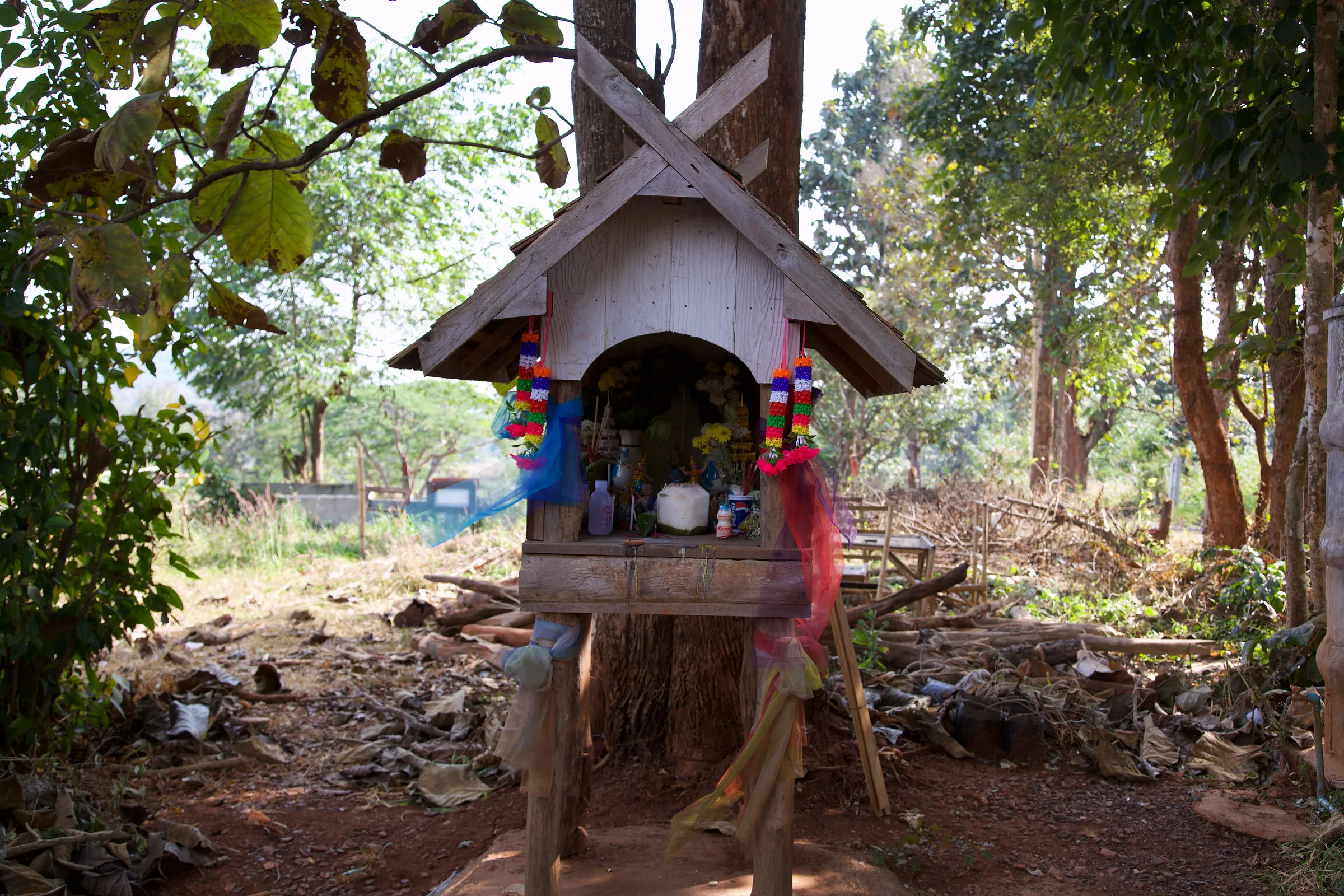 A small spirit house on a post among trees.