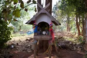 A small spirit house on a post among trees.