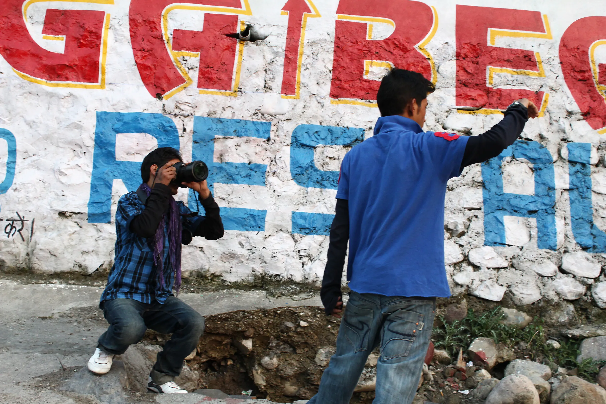 Two young people photographing in front of a large painted sign.