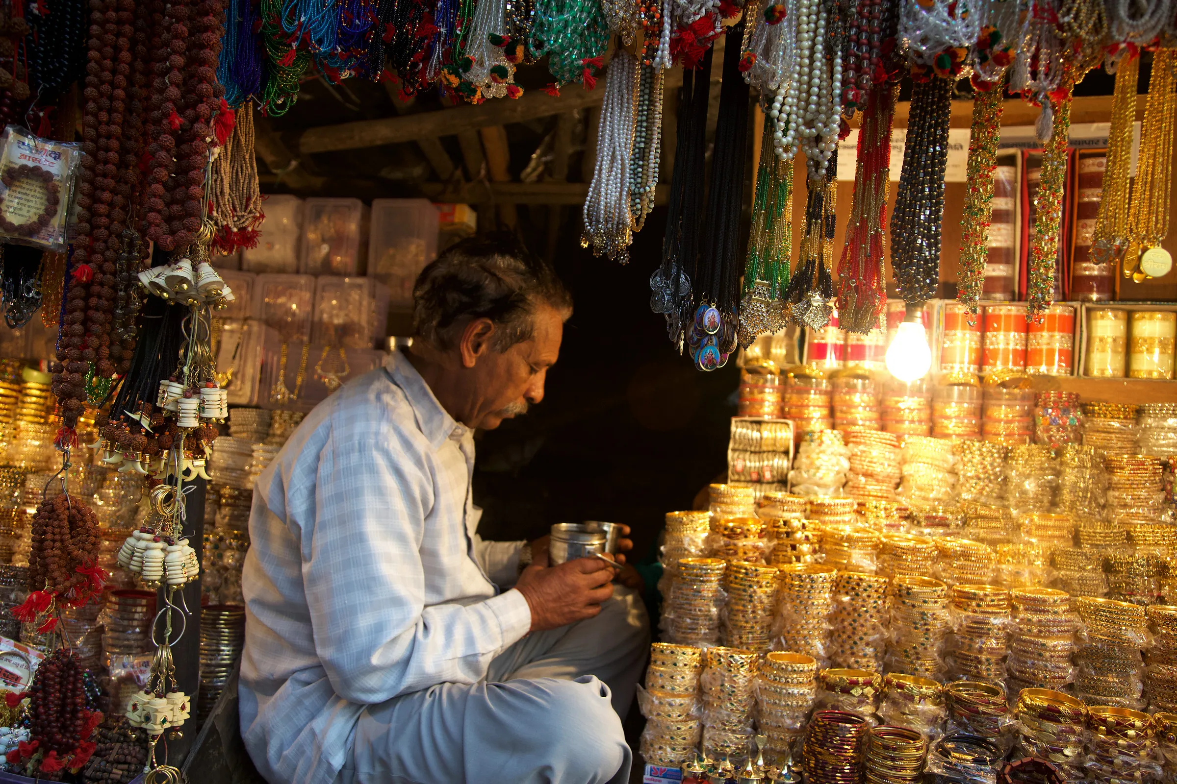 A man seated among shelves of bangles in a shop.